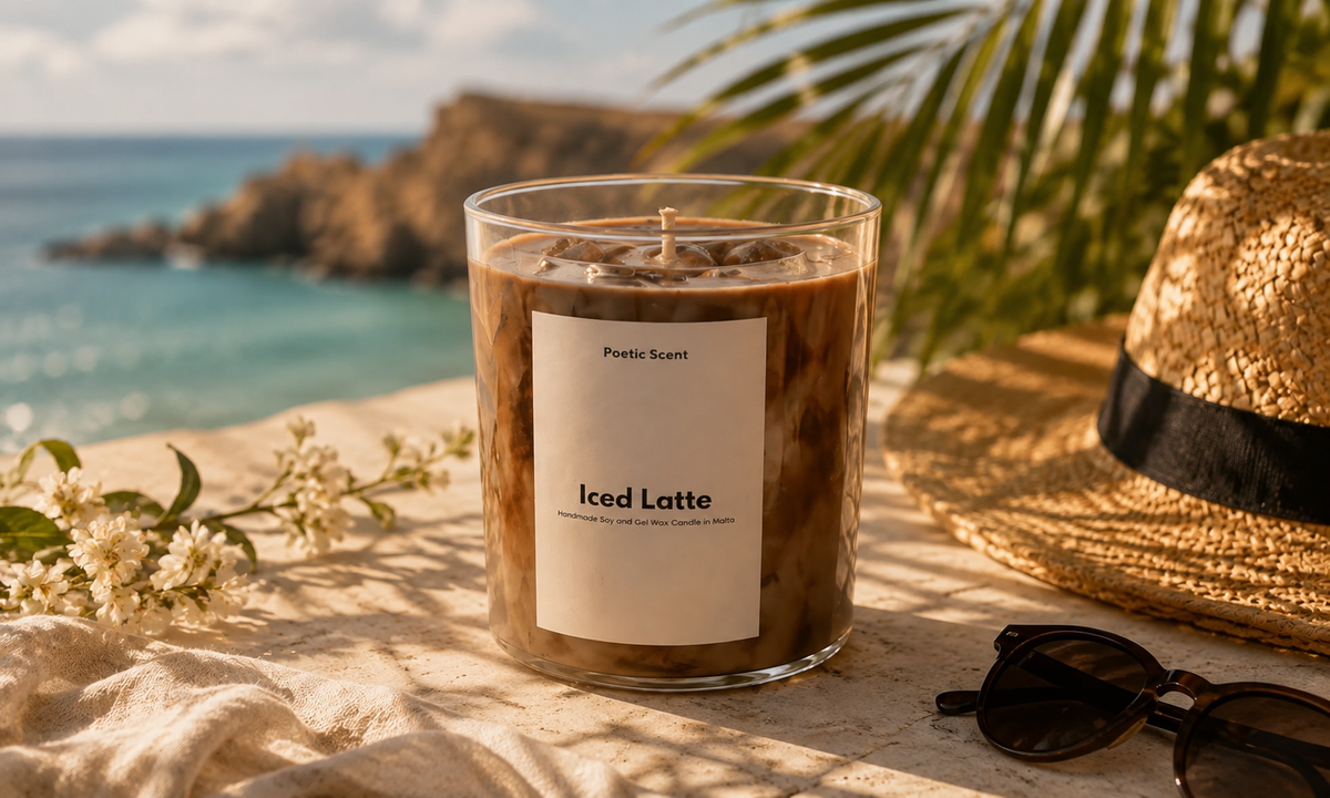 A large glass jar candle labeled 'Iced Latte' by Poptic Scent sits on a beach-style surface with the ocean, rocks, palm leaves, a straw hat, and sunglasses in the background.